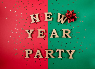 Yeşil ve kırmızı bir zemin ve üstünde de Yeni Yıl Partisi yazan kırmızı bir fiyonk. Harfler ahşaptan yapılmış ve arka plana saçılmış.