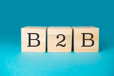 Üç tahta blokta B2B yazıyor. Bloklar öyle bir düzenlenmiş ki kelimeyi heceliyorlar. Soldaki ilk blok, ortadaki ikinci blok.