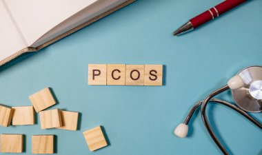 Üzerinde PCOS harfleri olan ahşap bir blok mavi bir yüzeyde, Polisistik Yumurtalık Sendromu 'nu ve sağlık farkındalığıyla olan bağlantısını sembolize ediyor..
