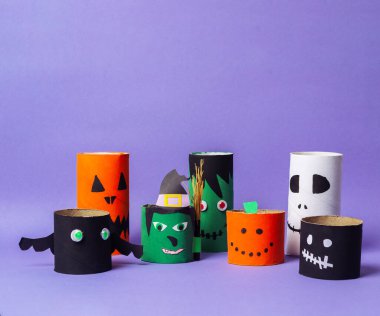 Cadılar Bayramı temalı bir grup kağıt tüp mor bir arka plan üzerine dizilmiş. Tüplerde cadı, iskelet ve balkabağı gibi çeşitli karakterler yer alıyor. Sahne şenlikli ve eğlenceli.