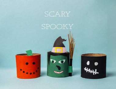 Cadılar Bayramı temalı üç fener, bir cadı, bir balkabağı ve bir iskeletle. Fenerler sıraya dizildi ve arka plan mavi.