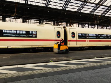 Köln, Almanya - 19 Mart 2022 - Sarı ve turuncu takım elbiseli bir adamın önünde küçük bir araç sürdüğü bir tren