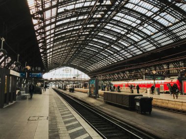 Köln, Almanya - 19 Mart 2022 - Demiryolu üzerinde kırmızı bir tren istasyonu. İstasyon birkaç kişi dışında boş.