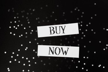 Buy now is written on a black background with stars. Concept of urgency and excitement, as if the viewer is being encouraged to make a purchase immediately clipart