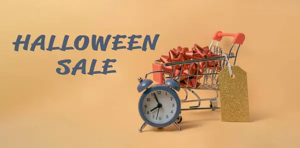 Üzerinde Cadılar Bayramı İndirimi yazan saati olan bir alışveriş arabası. Alışveriş arabası Cadılar Bayramı temalı eşyalar ile süslenir, örneğin bir balkabağı ve biraz kırmızı