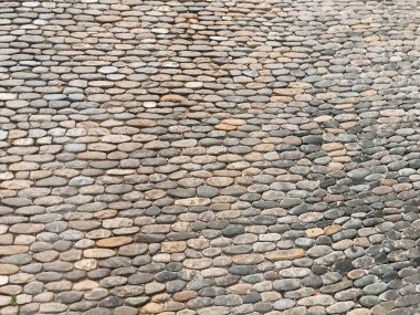 Küçük taşlar desenli taş bir duvar. Duvar gri ve kahverengi renkli. Taşlar, derinlik ve doku hissi yaratacak şekilde sıralanmış.