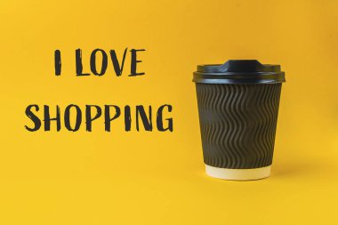 Siyah kapaklı kahve fincanı sarı arka planda duruyor. Altında 