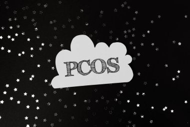 Yıldızlı bir gökyüzünün siyah ve beyaz görüntüsü. Beyaz harflerle yazılmış Pcos kelimesi. Karanlık gökyüzünde parlayan yıldızlar gibi gizem ve merak kavramı
