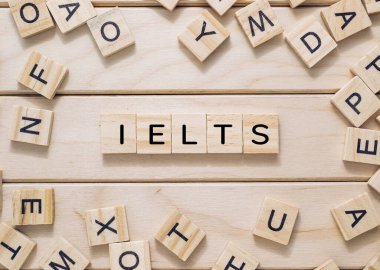Görüntü, genellikle akademik veya göçmenlik amaçlı olarak kullanılan Uluslararası İngilizce Dil Test Sistemi 'ni sembolize ederek IELTS' i heceleyen ahşap bloklardan oluşan bir kolaj içeriyor..