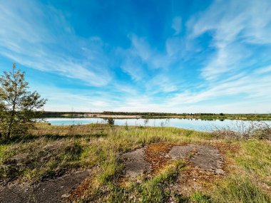 Güzel mavi gökyüzü, birkaç bulut ve arka planda bir göl. Gökyüzü açık ve göl sakin.