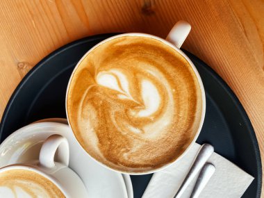 Tepsinin üzerinde krema kıvrımlı bir fincan kahve duruyor. Tepside bir peçete ve çatal da var. Rahatlık ve rahatlama kavramı, çünkü kahve sıcacık ile ilişkilendirilir.