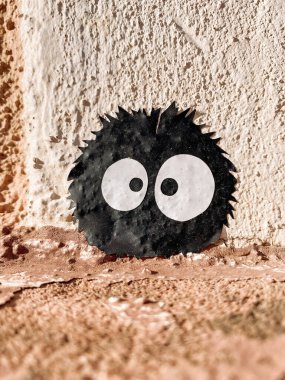 Büyük gözlü küçük siyah beyaz yaratık bir duvarda oturuyor. Yaratığın ürkütücü bir görüntüsü var ve kameraya bakıyor gibi görünüyor.