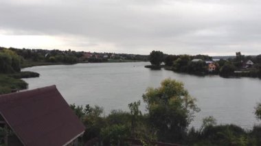 Arka planda bir ev olan göl. Gökyüzü bulutlu ve su sakin. Huzurlu ve huzurlu bir sahne.