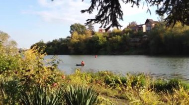 Arka planda birkaç ağaç olan göl. Su sakin ve berrak. Suda bir insan var ve suda birkaç tekne var.