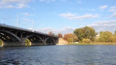 Köprü, üzerinde açık mavi bir gökyüzü olan bir nehri kapsar. Köprü, arka planda birkaç ağaç bulunan büyük bir yapıdır.