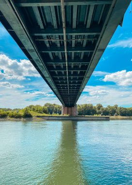 Köprü, arka planda mavi gökyüzü olan bir nehri kapsar. Köprü yukarıdan görünen büyük bir yapıdır.