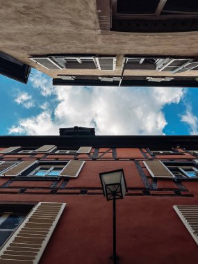 Bulutlu bir gökyüzü ve lamba direği olan bir şehrin sokak manzarası. Sokak pencereli ve panjurlu binalarla dolu.