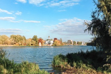 Arka planda yeşil ağaç olan bir su kütlesi. Su sakin ve berrak. Uzakta bazı binalar var.
