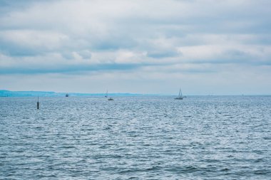 İçinde birkaç tekne olan bir su kütlesi. Su sakin ve berrak. Gökyüzü bulutlu ve güneş görünmüyor.