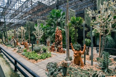 Bahçede bitkiler ve heykeller var. Bahçede bir sürü ağaç ve çalı var.