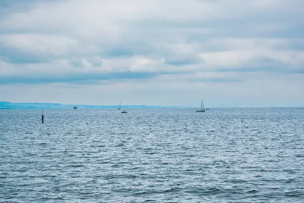 İçinde birkaç tekne olan bir su kütlesi. Su sakin ve berrak. Gökyüzü bulutlu ve güneş görünmüyor.
