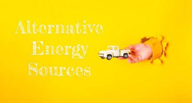 Altında Alternatif Enerji Kaynakları yazan bir oyuncak kamyonu tutuyordu. İmajın eğlenceli ve eğitici bir havası var.