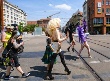 Karlsruhe, Almanya - 3 Haziran 2023 - Bir grup insan, büyük bir peruk ve mor tüylü bir başlık takan bir sokakta yürüyorlar.