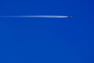 Mavi gökyüzünde buhar izleri olan bir yolcu uçağı.