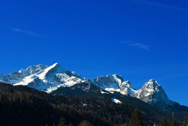 snow-covered Wetterstein mountains in spring, with Alpspitze on the left, Zugspitze in the center and Waxenstein on the right, seen from Klais, Bavaria, Germany clipart