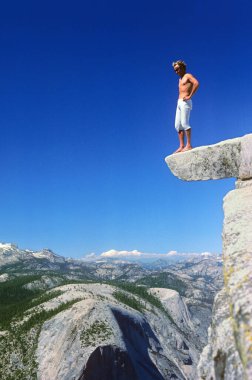 a man takes a test of courage and stands on a ledge at the top of the Half Dome, 600 meters above the ground, Yosemite Valley, California, USA clipart