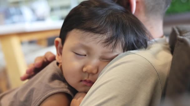 小さな少年が父親の肩で眠っている アジアの少年 男の子は父親の腕の中で安全だと感じています 疲れた息子を抱えている父親 — ストック動画