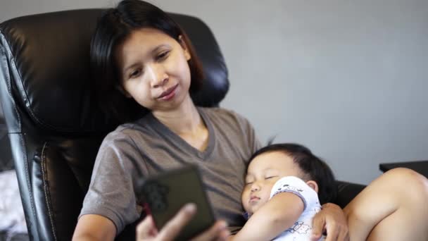 Mamma Sitter Fåtölj Hålla Little Sleepy Son Används Smartphone Hemma — Stockvideo
