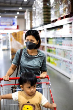 Anne, küçük bebeğiyle alışveriş arabasını süpermarket koridorunda itiyor. Anne ve Oğlu süpermarkette. Çocuk konseptiyle alışveriş.. 