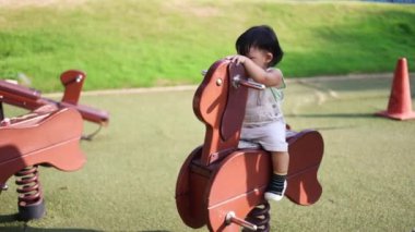 Parktaki bebek. Bebek çocuk, oyun bahçesinde sallanan at oyuncağında sallanıyor. Mutlu aile bir çocuk hayali konsepti. Bebek bebek doğayla oynuyor Oyuncak atın üstünde sallanıyor. 