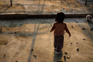 Asyalı çocuk çimento zeminde futbol oynuyor. Çocuk dışarıda oynuyor. Arka taraftan çekilmiş..