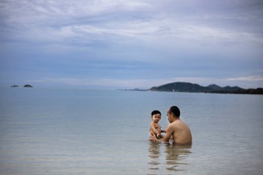 Baba ve oğul denizde yüzerken eğleniyorlar. Baba oğluna yüzmeyi öğretiyor..