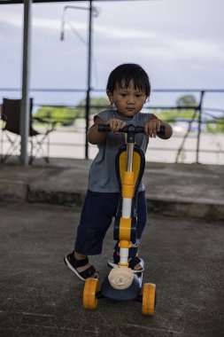 Photography of toddler determined while holding scooter, capturing energy and growth, suitable for parenting ads, lifestyle promotions, and childhood storytelling visuals.