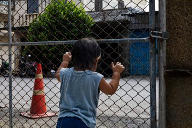 Curious toddler grabbing fence bars with innocent look, emotional photography ideal for parenting ads, family campaigns, lifestyle visuals, and creative media storytelling.