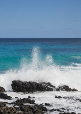 Ön planda volkanik kayalar ve arka planda deniz ve gökyüzü ile kıyıda fren yapıyor.