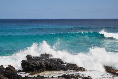 Ön planda volkanik kayalar ve arka planda deniz ve gökyüzü ile kıyıda fren yapıyor.