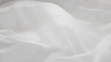 Yumuşak, akışkan beyaz kumaşın yumuşak dalgaları ve kıvrımlarıyla yakın çekim görüntüsü, sakin ve zarif bir atmosfer yaratıyor..