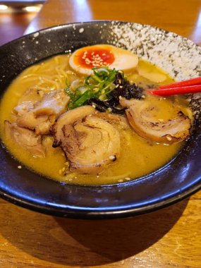 Miso tori paitan ramen ile kalın baharatlı tavuk çorbası ızgara tavuk dilimleri ve ahşap masada izole edilmiş siyah kasede yumurta..