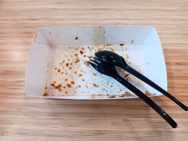 Tahta arka planda siyah plastik kaşık ve çatallı boş beslenme çantası kağıdı..