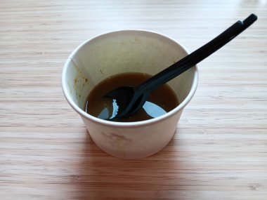 Endonezya 'dan arta kalan soto ayam ya da tahta arka planda siyah plastik kaşık ve çatalla karton kasede tavuk çorbası. Yiyecek atığı konsepti.