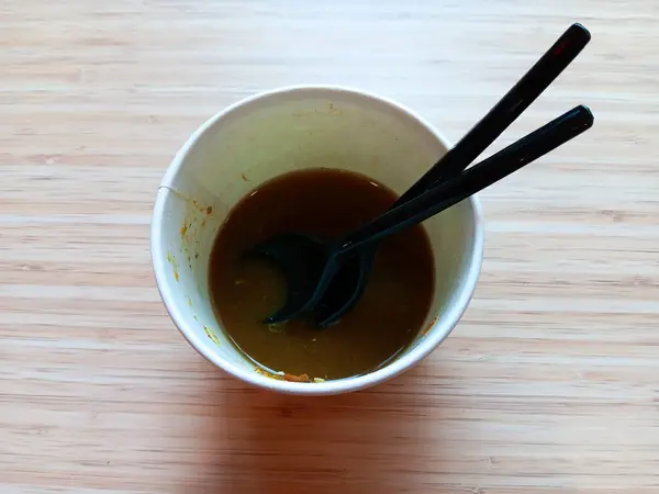 Endonezya 'dan arta kalan soto ayam ya da tahta arka planda siyah plastik kaşık ve çatalla karton kasede tavuk çorbası. Yiyecek atığı konsepti.