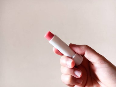 Beyaz arka planda pembe dudak kremi tutan kadın..