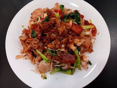 Çin yemeği Kızarmış Düz Pirinç Eriştesi (kway teow), karides, sığır köftesi, lapa cheong veya Çin sosisi ve siyah arka planda izole edilmiş beyaz tabak üzerine kırmızı domuz eti..