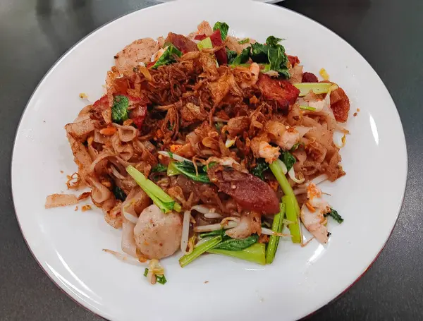 Çin yemeği Kızarmış Düz Pirinç Eriştesi (kway teow), karides, sığır köftesi, lapa cheong veya Çin sosisi ve siyah arka planda izole edilmiş beyaz tabak üzerine kırmızı domuz eti..