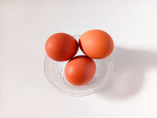 Şeffaf kâse üzerinde kahverengi kabuklu üç haşlanmış yumurta beyaz arka planda izole edilmiş..