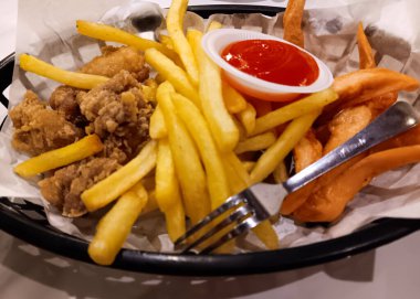 Kızarmış tavuk, patates kızartması, acı soslu sosis ve beyaz arka planda izole edilmiş bir sepet..